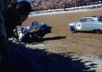 Joie Ray is assisted from his overturned Henry J as Pepper Cunningham's Hudson passes...